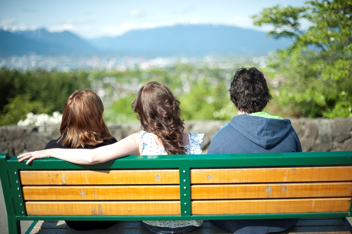 Three people sitting on a bench looking at a view of hills